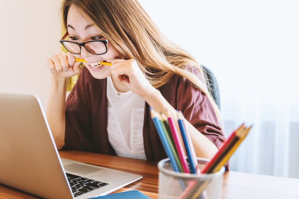 woman biting pencil while sitting on chair in front of computer during daytime while searching for excellent web hosting
